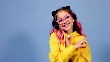 a girl in a yellow hoodie and blue shorts is dancing in front of a blue wall