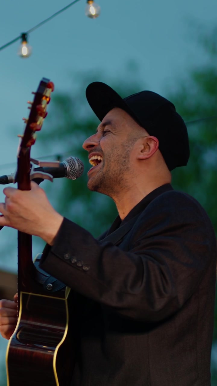 Mann som synger og spiller akustisk gitar på en utendørs kveldskonsert
