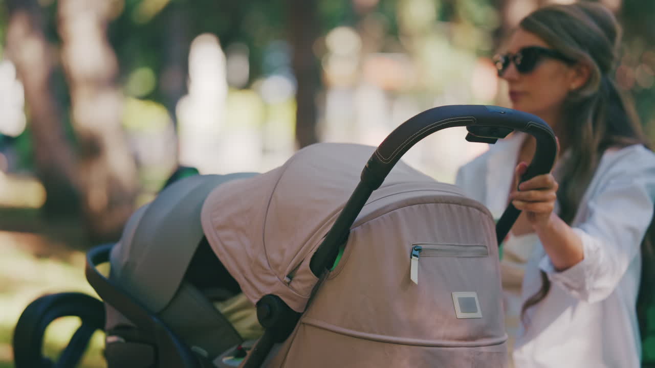 Young mother sitting on a park bench next to a stroller, enjoying a peaceful outdoor moment with her baby