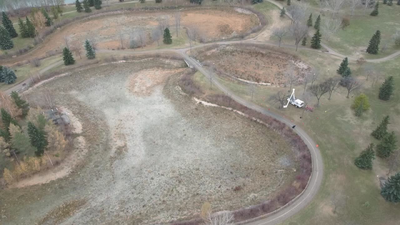 elevación aérea ojo de pájaro volar sobre estanques secos lagunas poda de árboles poda hombre ascensor brazo articulado plataforma de trabajo camión en la tarde de otoño con pinos dispersos árboles desnudos variados caminos vacíos2-3