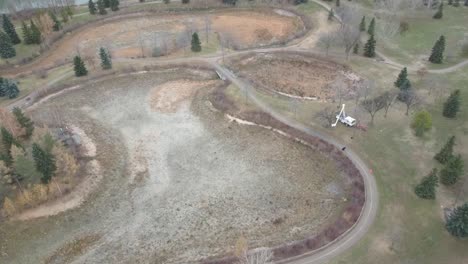 aerial-rise-birds-eye-fly-over-dried-up-ponds-lagoons-tree-trimming-pruning-man-lift-articulated-arm-work-platform-truck-on-fall-afternoon-with-scattered-pine-trees-bare-varying-trees-empty-paths2-3