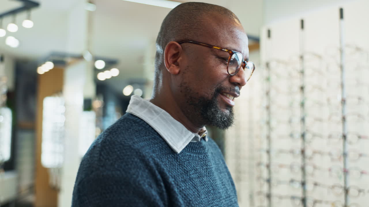 A man in a blue sweater and glasses uses a tablet in an optician's store