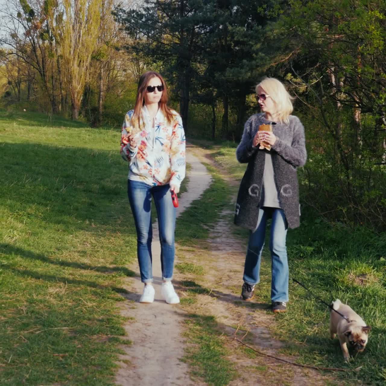 dos mujeres paseando por el parque con su perro