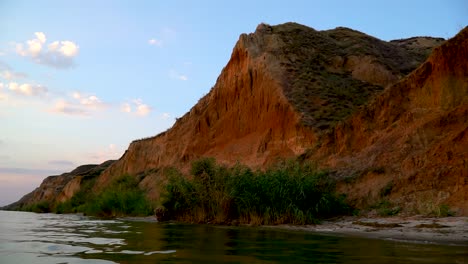 Static-shot-of-red-cliffs-,-green-bushes,-blue-sky-and-the-sea-in-foreground