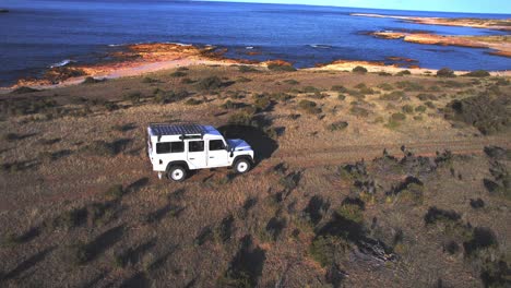 rastreando un vehículo todoterreno mientras pasa por el camino de tierra junto al mar a través de las llanuras de hierba corta bahía bustamante