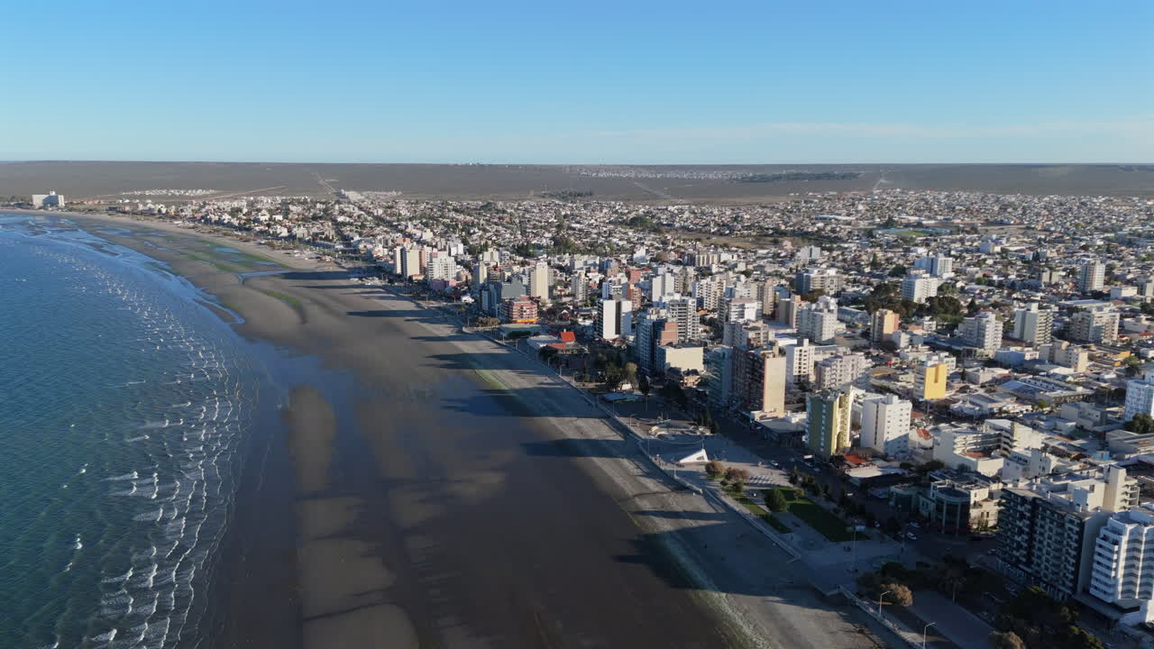 Aerial shot of the city of Puerto Madryn, Patagonia, Argentina. Overflight over the coastal buildings casting sunset shadows on the sand.