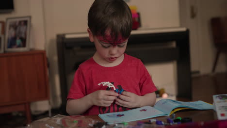 un lindo bebé con la frente diseñada con una camiseta roja con un boceto de dos pájaros abre un libro de dibujo y participa en una obra de arte