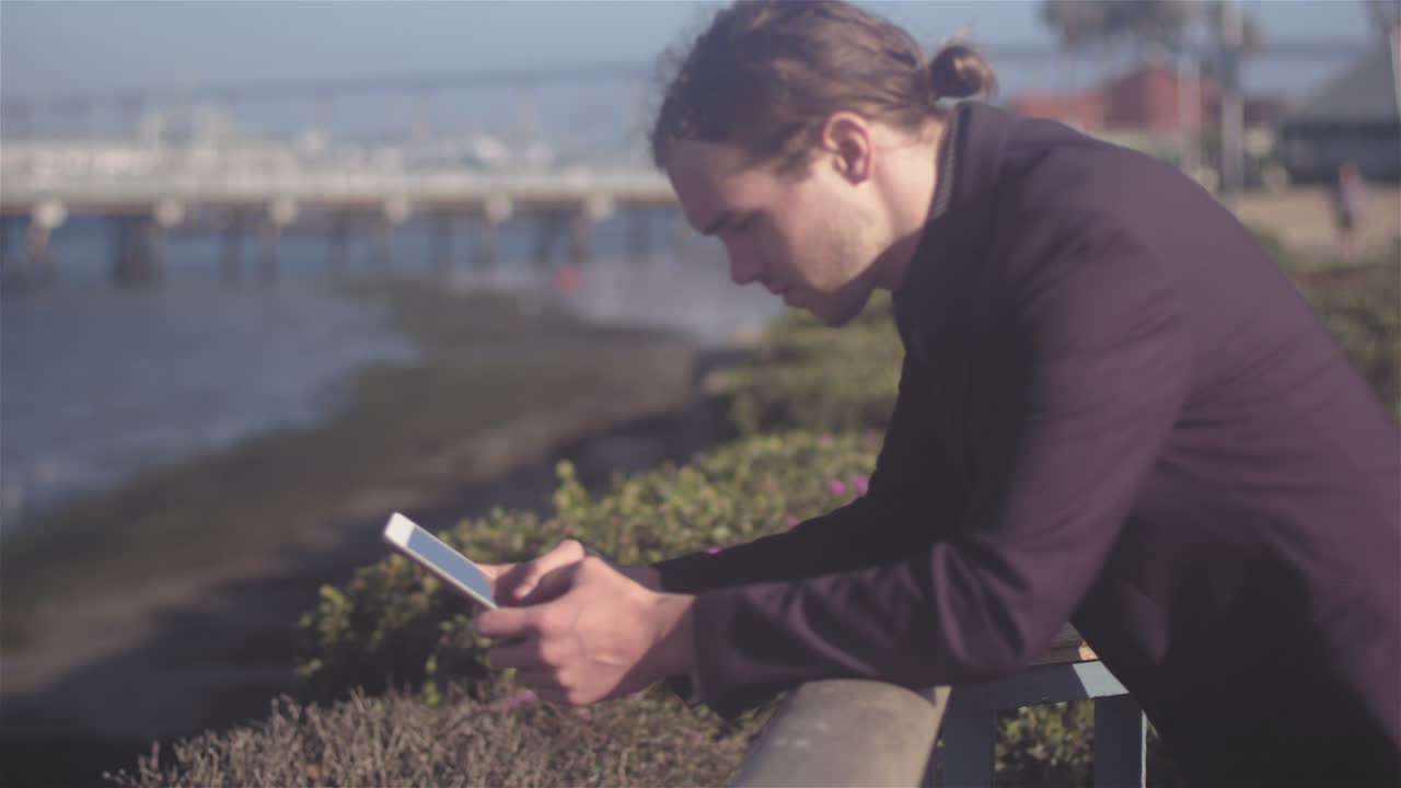 Focusing shot of a young business man leaning up against a rail, while using his tablet