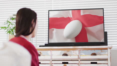 Mujer-Caucásica-Viendo-Televisión-Con-Una-Pelota-De-Rugby-En-La-Bandera-De-Inglaterra-En-La-Pantalla