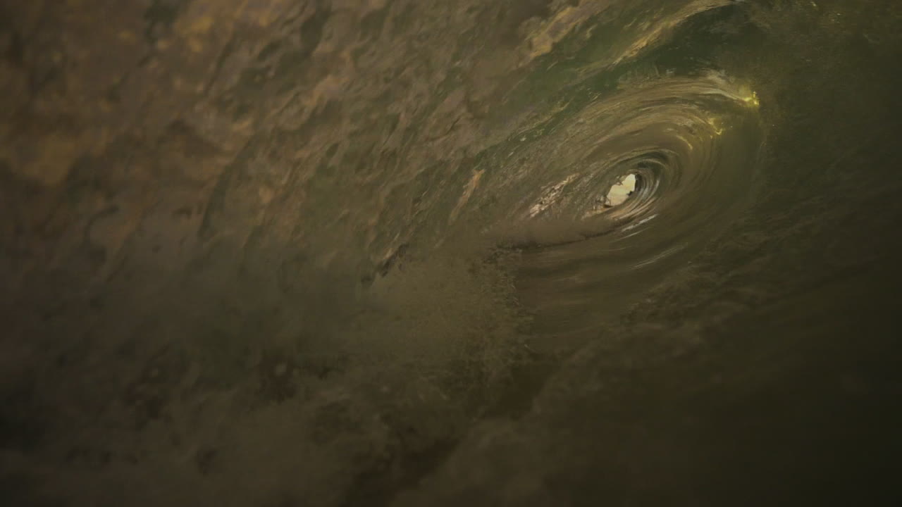 The camera captures the motion of water from inside the wave as it breaks, showcasing the swirling water and foam