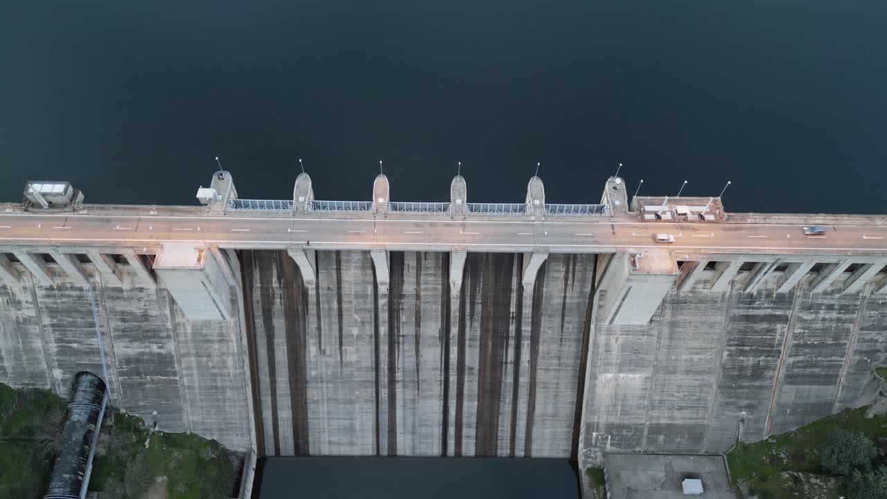 Fixed drone shot of cars driving over a dam at a reservoir in Cáceres, Spain. Infrastructure, nature, and rural activity