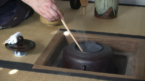 ladle of hot water is poured into japanese tea bowl during japanese tea ceremony