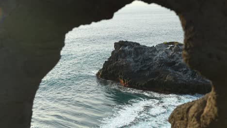 ocean waves crashing in slowmo into rocks, view through natural rock window