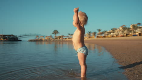 Cute-little-baby-boy-walking-along-sunny-coastline-at-summer-day.