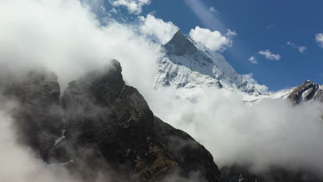 aerial drone shot going around clouds to reveal snow topped mountain in the annapurna mountains, nepal