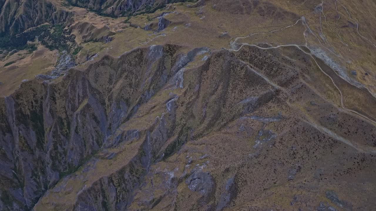 Aerial drone footage performing a tilt-up over Roys Peak hiking trail in Wanaka, New Zealand, revealing Lake Wanaka and surrounding mountain scenery