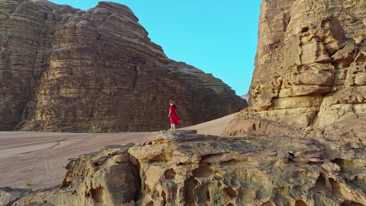 mujer con vestido rojo de pie en la roca disfrutando del aire fresco en el desierto de wadi rum en jordania