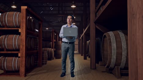 full body of an asian male professional worker with his laptop in cellar of winery, he observes by looking around before he come to concentrating with his laptop