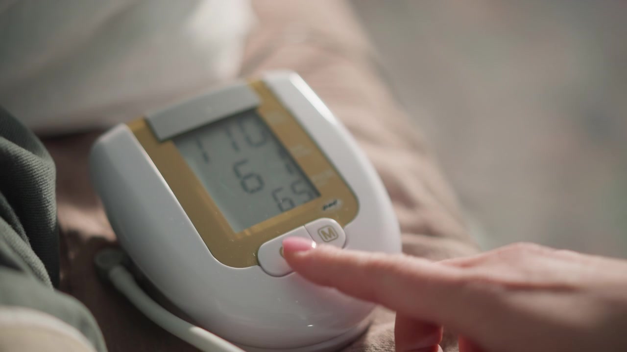 Braccio di un uomo di colore, lettura del display del monitor digitale controllata con la pressione di un dito, chiara lettura numerica dei parametri vitali, richiamo e conferma della memoria, momento tranquillo al capezzale durante un controllo sanitario a domicilio.