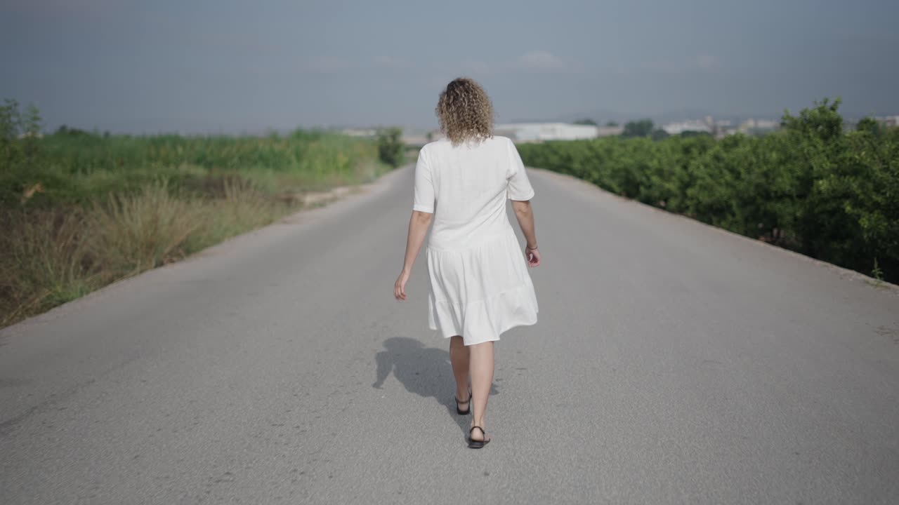 Woman in a white dress walking on a country road