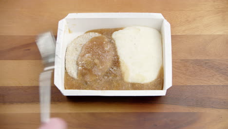 packed frozen food in a meal box plastic container, trying to break with a metal fork