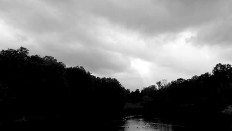 nubes oscuras cuelgan bajas sobre un lago misterioso y tranquilo recortado por un bosque blanco y negro, aéreo