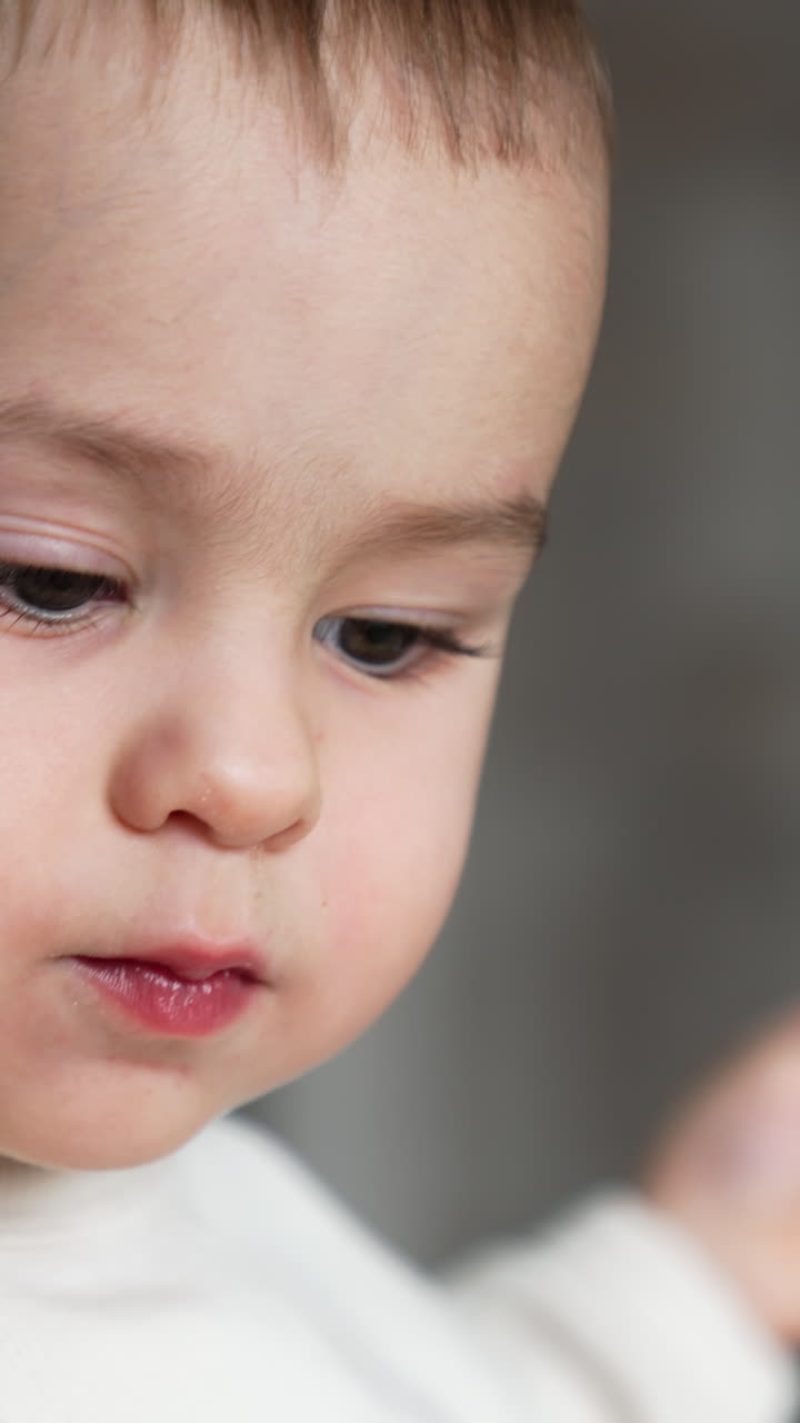 Cute face of an angelic Caucasian baby. Little boy showing tongue to the camera. Close up. Blurred backdrop. Vertical video