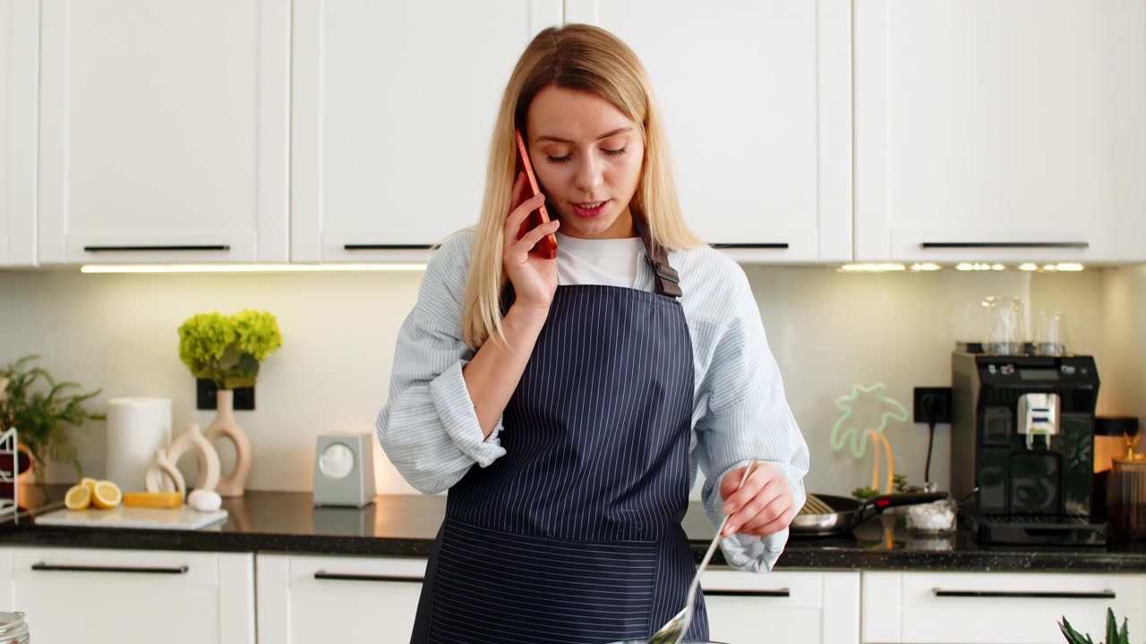 Giovane donna che parla al telefono mentre mescola l'insalata, condividendo una ricetta chetogenica per un pranzo fresco nella cucina di casa.