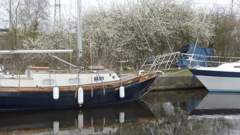 Kleine-Alte-Blaue-Segelboote,-Die-An-Einem-Schmalen-Ländlichen-Kanaljachthafen-Festgemacht-Sind