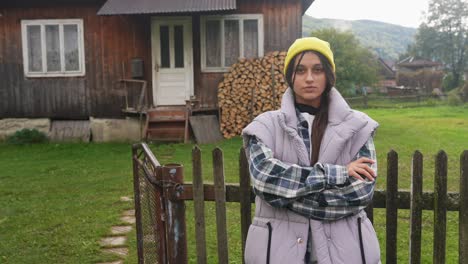 young woman standing by a wooden fence in front of a rural house