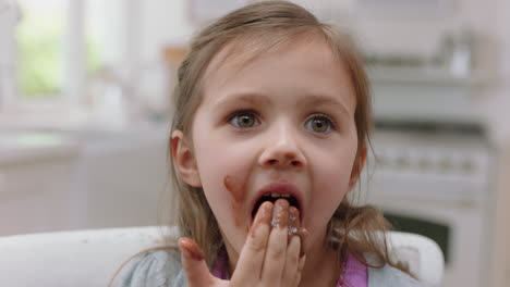 cute little girl with hands covered in chocolate licking fingers having fun baking in kitchen naughty child enjoying tasty treat at home