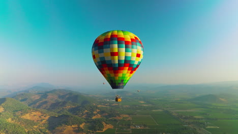 bright colorful hot air balloon descending in the blue sky. aerostats soaring over the hazy mountains on sunny day. top view.