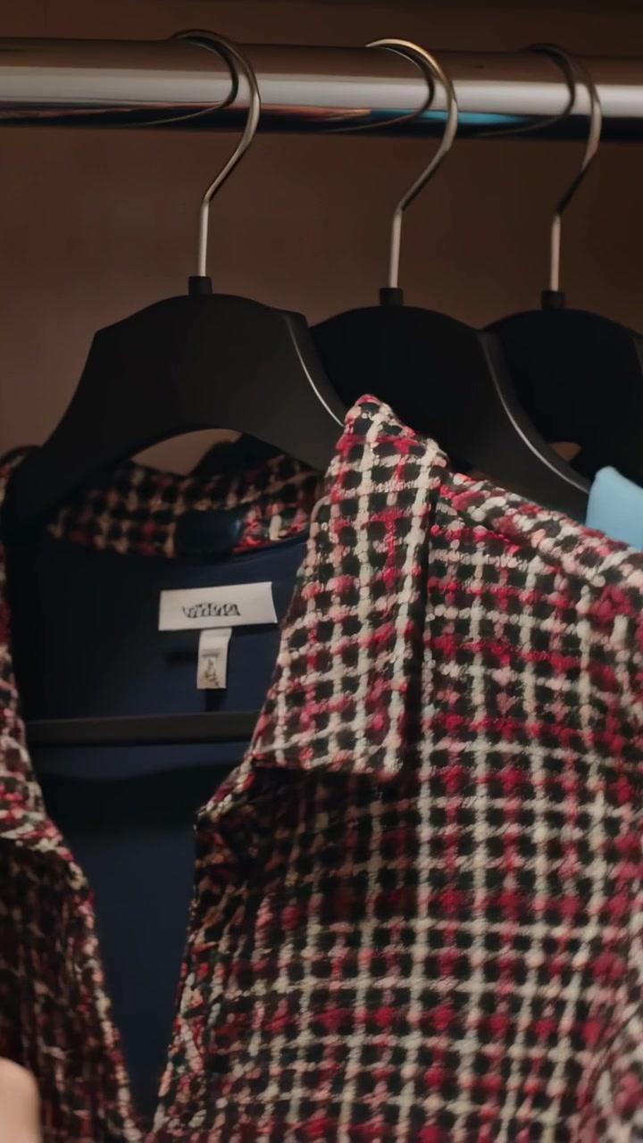 Vertical video: Entering bare hand from bottom sliding rail in closet feeling shirts selecting coat