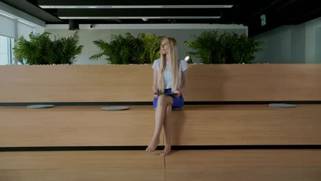relaxing woman with tablet in office. young elegant woman sitting barefoot on wooden tribune in modern office using tablet and taking rest