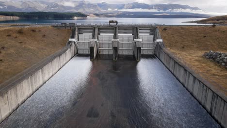 agua que sale de la presa hidroeléctrica en el lago pukaki, montañas en el fondo