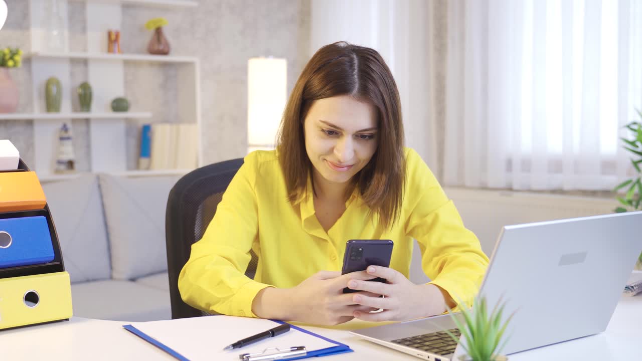 mujer joven feliz usando el teléfono en el escritorio de la oficina de casa.