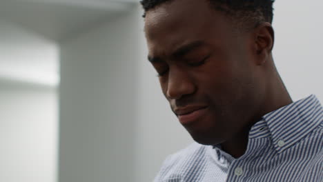 close up of young man with mental health issues standing in office looking depressed and unhappy with head in hands