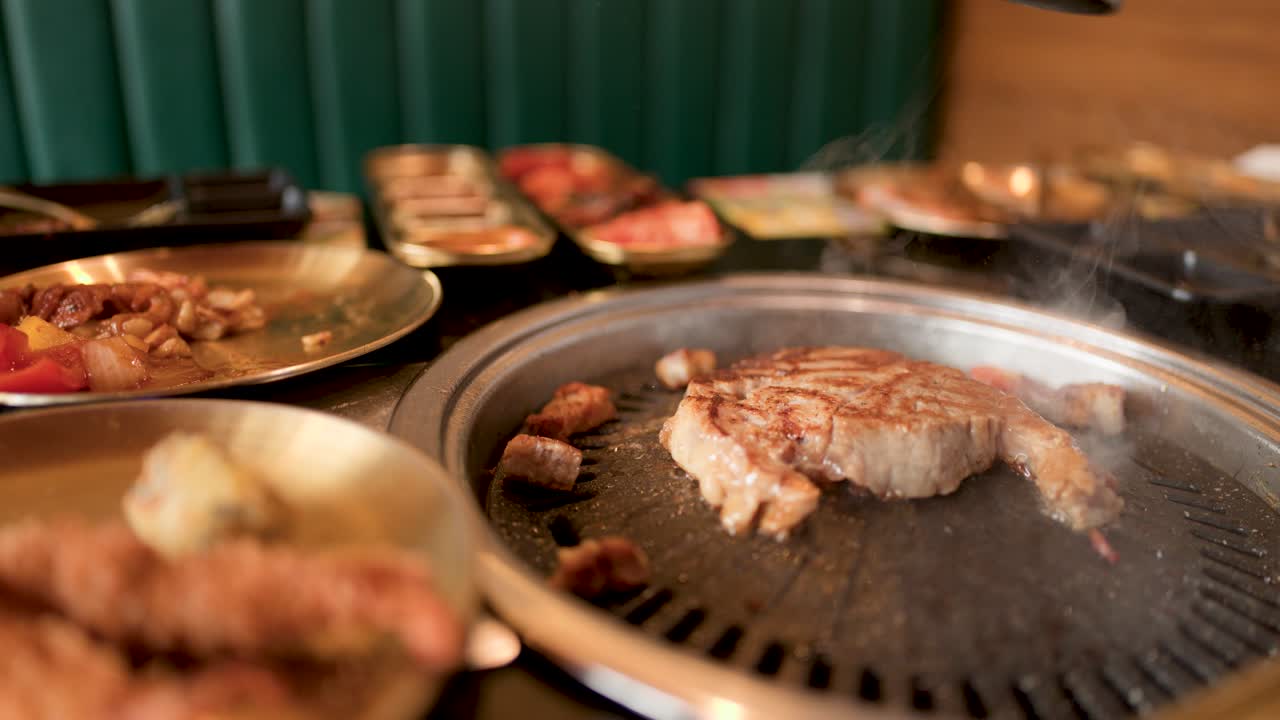 Pork belly sizzles on tabletop grill surrounded by side dishes in warmly lit restaurant setting