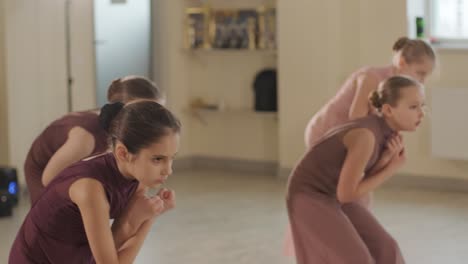 un grupo de jóvenes estudiantes de ballet con ropa de baile negra practicando posiciones en un amplio estudio de ballet con pisos de madera y barras montadas en la pared. expresiones enfocadas y movimientos sincronizados.