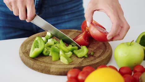 the girl slices the red tomato for salad on the kitchen board with vegetables for vegetarian food