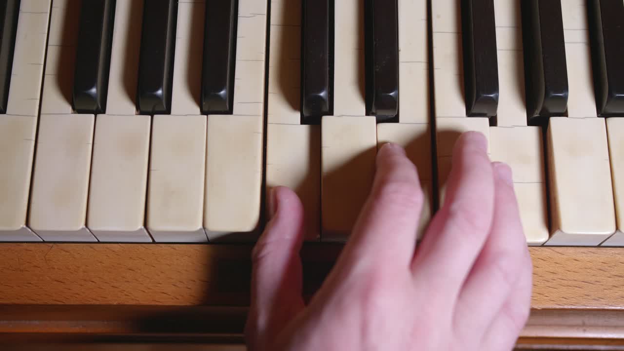 fotografía cenital de una mano tocando dos acordes en un piano antiguo