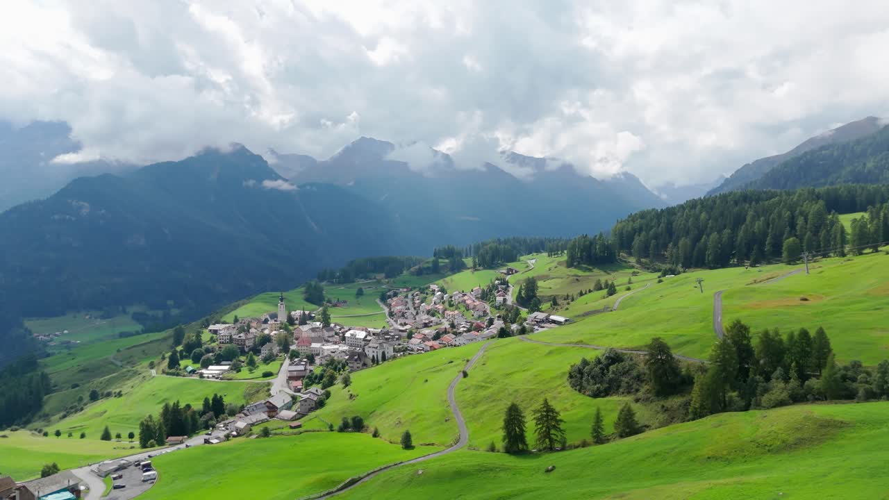 Cloudy day over idyllic small town in Switzerland. Aerial wide shot. Neighborhood with church on green steep hills of alps. Peaceful scene in summer