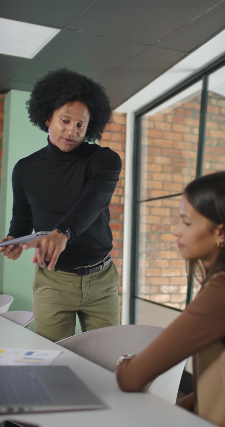 Vídeo vertical: Equipe afro-americana observando homem entrando com tablet e apontando para laptop na mesa