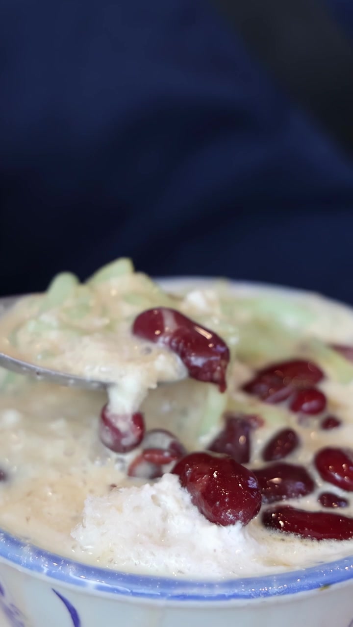 Close-up tangan menyendok es cendol dengan kacang merah, es serut, dan santan