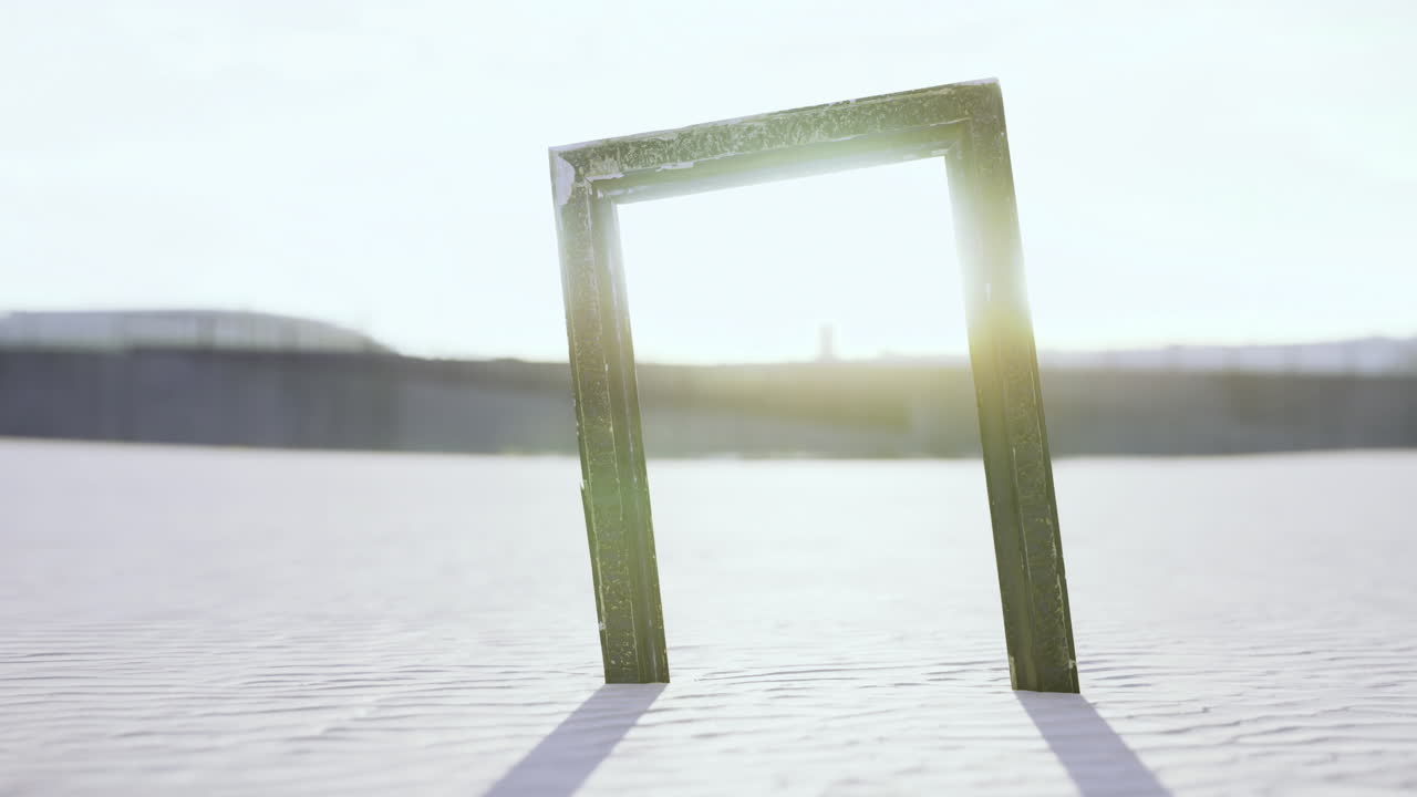 Sunlight beams through an empty frame on the sandy beach at dusk