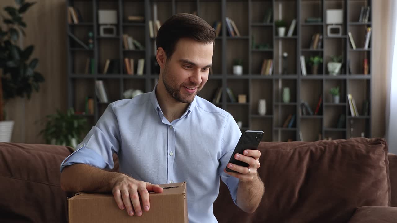 Hombre usando un smartphone mientras está sentado en un sofá con una caja de paquetería