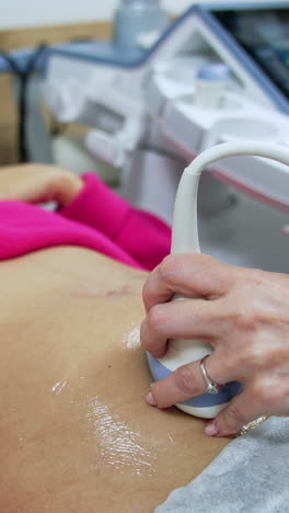 beautiful smiling lady lies having ultrasound examination. doctor's hand holds the ultrasonic device on woman's belly. close up.. vertical video