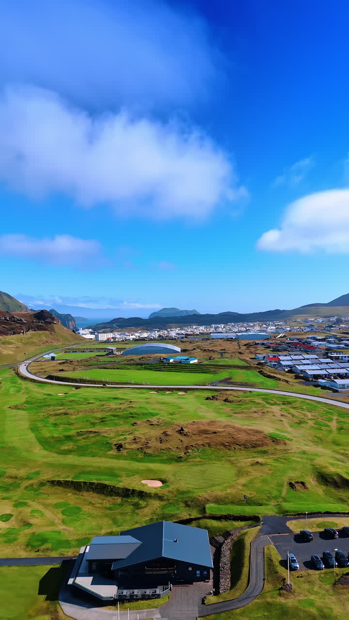 Green valley in the mountains with a village or little town. Sunny day footage in Iceland. Aerial view. Vertical video.