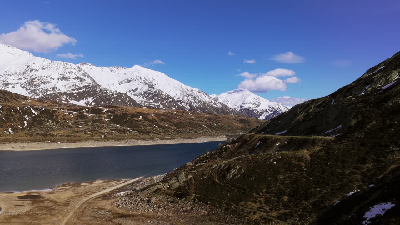 View of a serene mountain lake framed by rugged snowy peaks and grassy slopes.