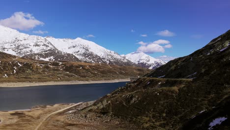 view of a serene mountain lake framed by rugged snowy peaks and grassy slopes.